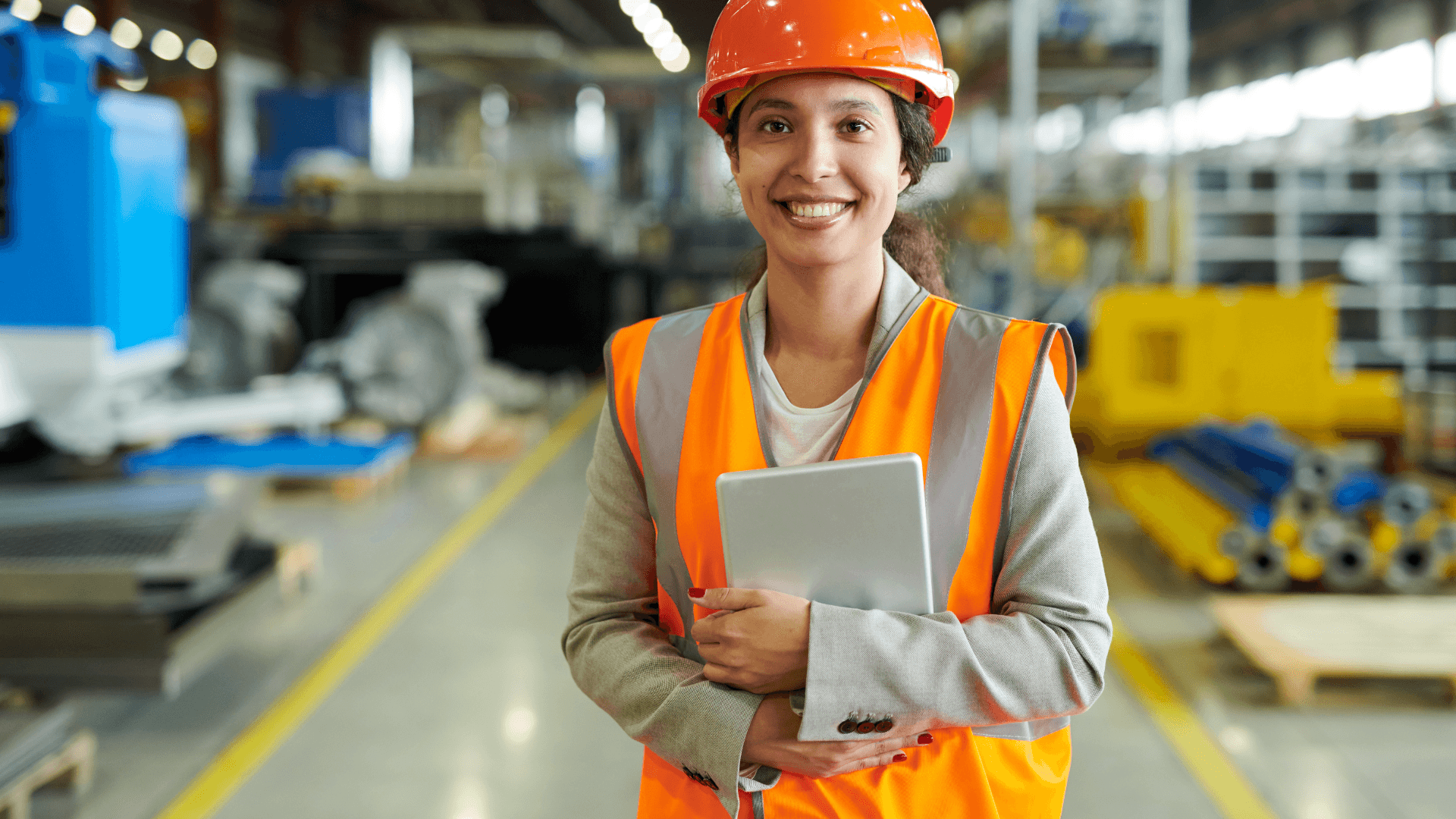 this image shows a woman worker in factory dressed in her safety gear and holding a tab.